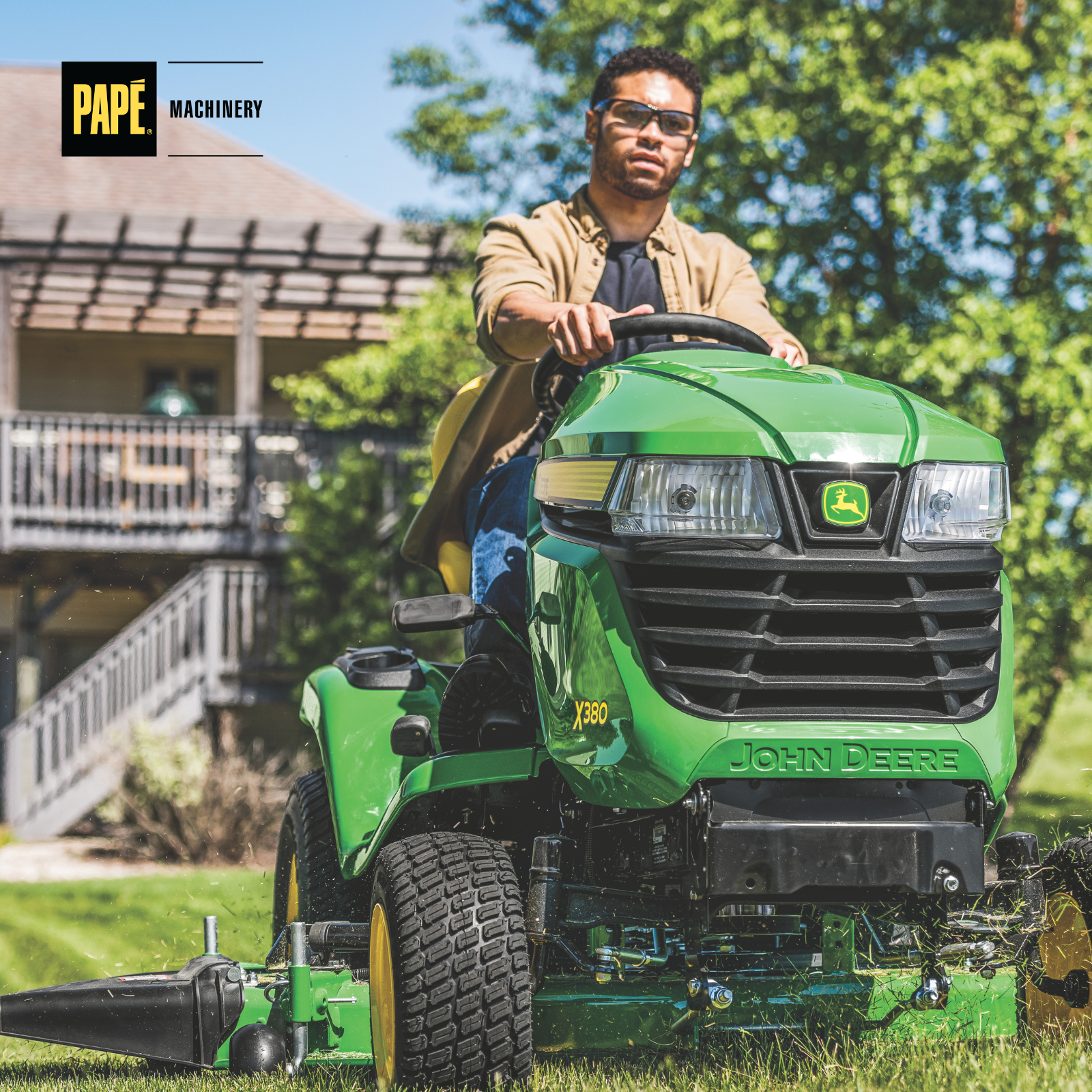John Deere X380 Select Series riding mower cutting grass on a residential lawn with trees and landscaped yard