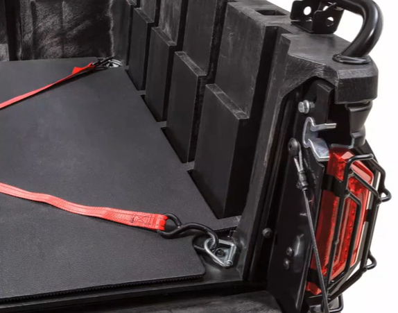 Truck bed with black tonneau cover secured by red straps and red tailgate light mounted on corner.