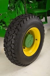 Black tread tire mounted on yellow-rimmed wheel against green machinery background.