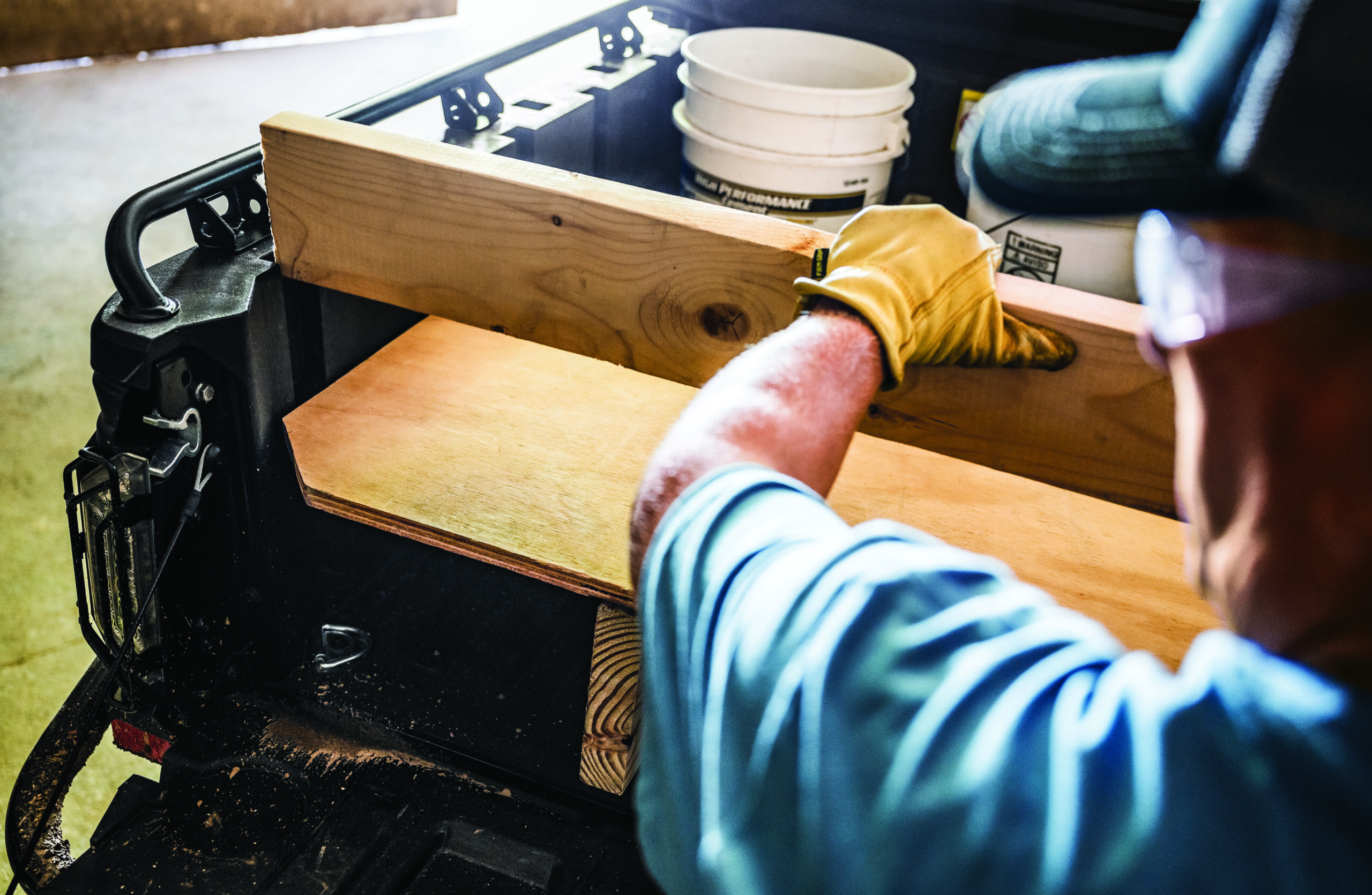 Worker in yellow glove and blue striped shirt reaching into a wooden-topped black tool organizer or cart containing white cups and supplies.