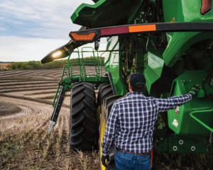Farmer inspecting a green combine harvester in a harvested crop field.