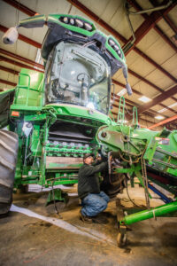 Technician working on the internal engine components of a green agricultural combine harvester in a workshop.
