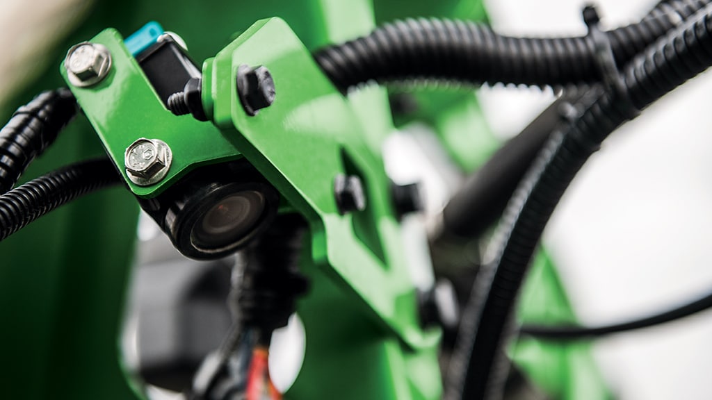 Close-up of a green mechanical brake caliper with black cables and metal adjustment bolts.