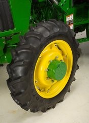 Large agricultural tractor tire with deep treads mounted on a yellow wheel rim against a green machine.