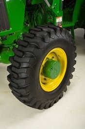 Large tread agricultural tire mounted on a yellow wheel rim, part of green farm equipment.