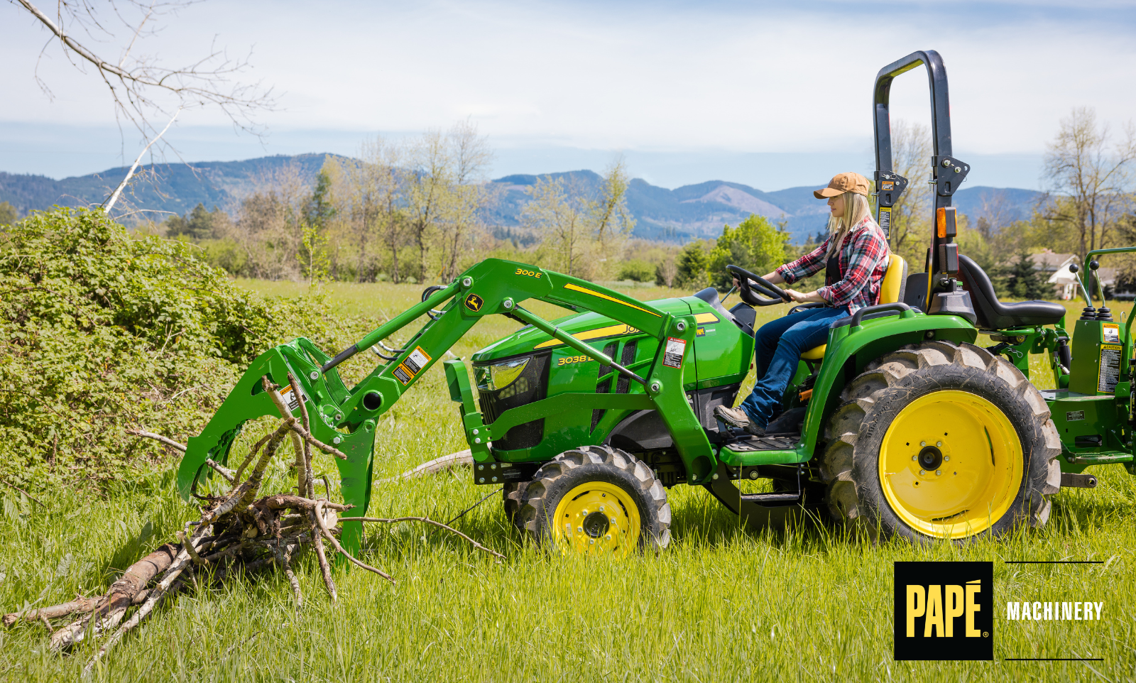 John Deere compact utility tractor clearing overgrown brush and tall grass with a rotary cutter to reclaim acreage for property maintenance