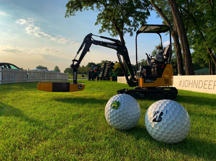 Two oversized golf balls on grass with compact excavators and equipment at a golf event or promotional display.